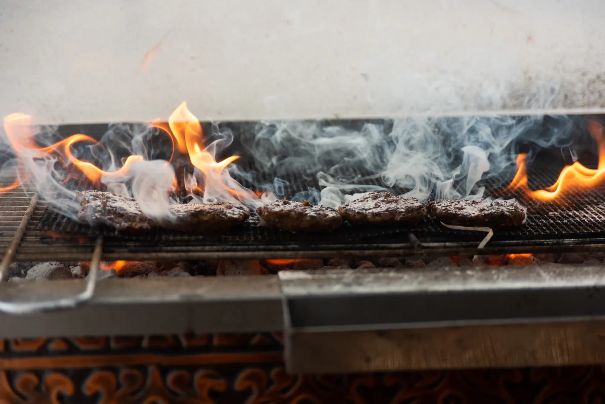 Flammen und Rauch über den Köfte auf dem Grill