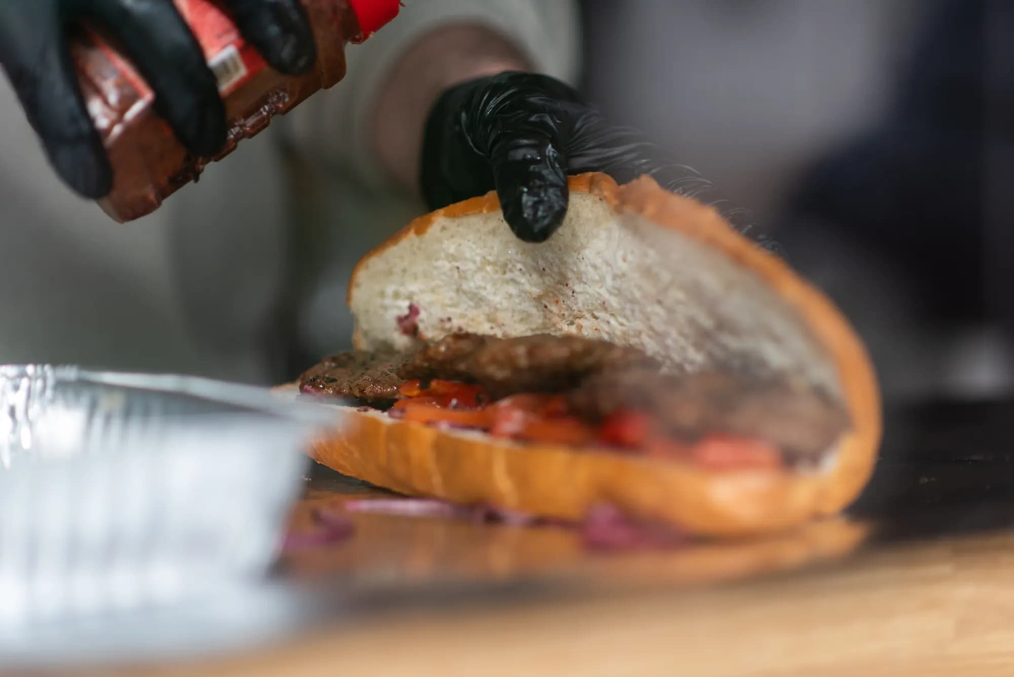 Sauce kommt auf ein Brot mit Köfte, Tomaten und Zwiebeln