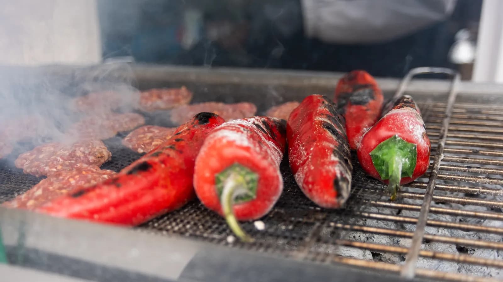 Gegrillte rote Peperoni und viele Köfte im Rauch auf dem Grillrost