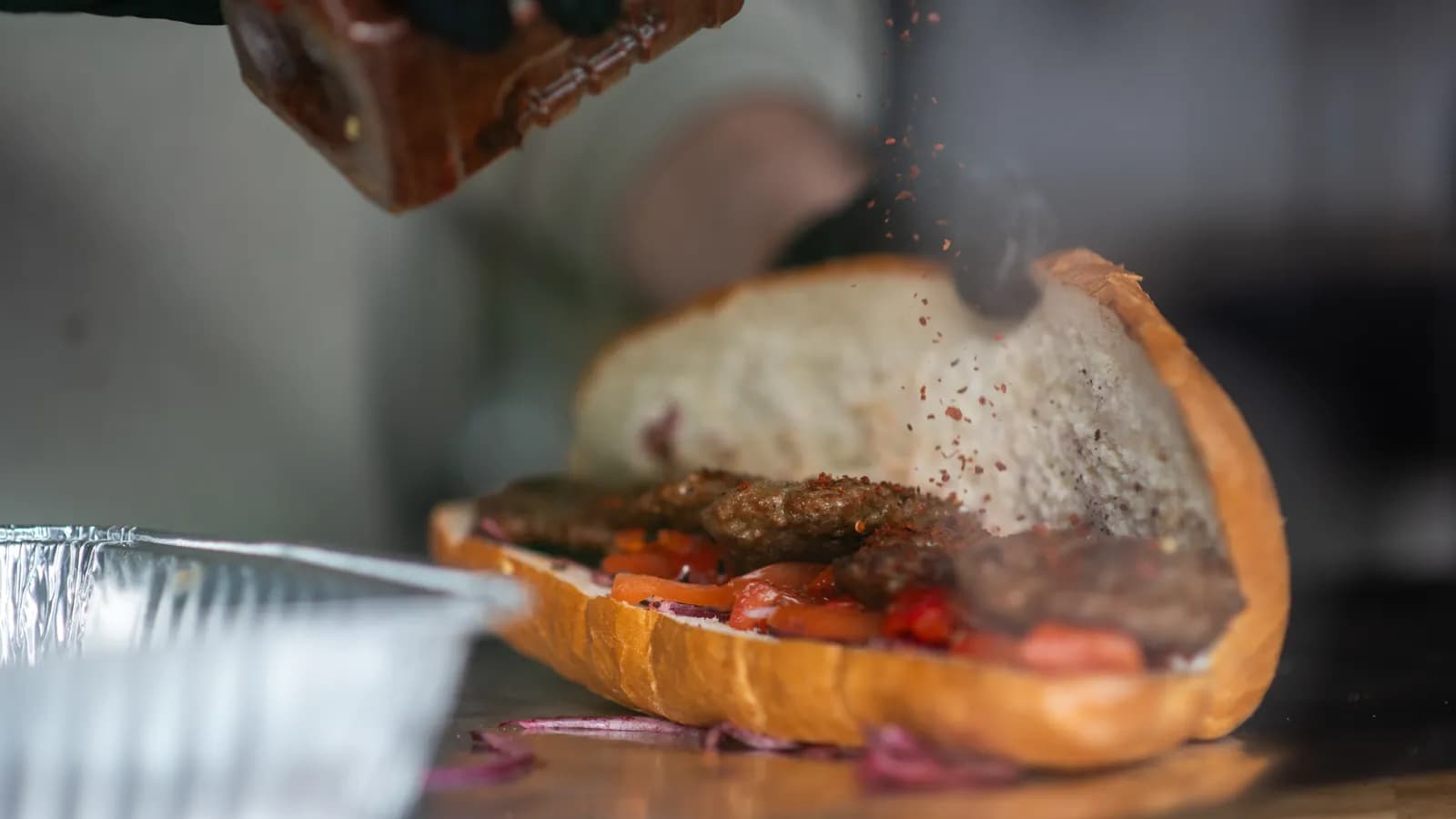 Ein Köfte-Brot mit Tomaten und Zwiebeln wird mit Gewürz bestreut