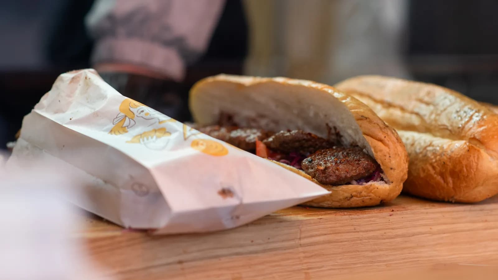 Zwei frische Köfte-Brote auf der Holztheke, eines in der Papiertüte