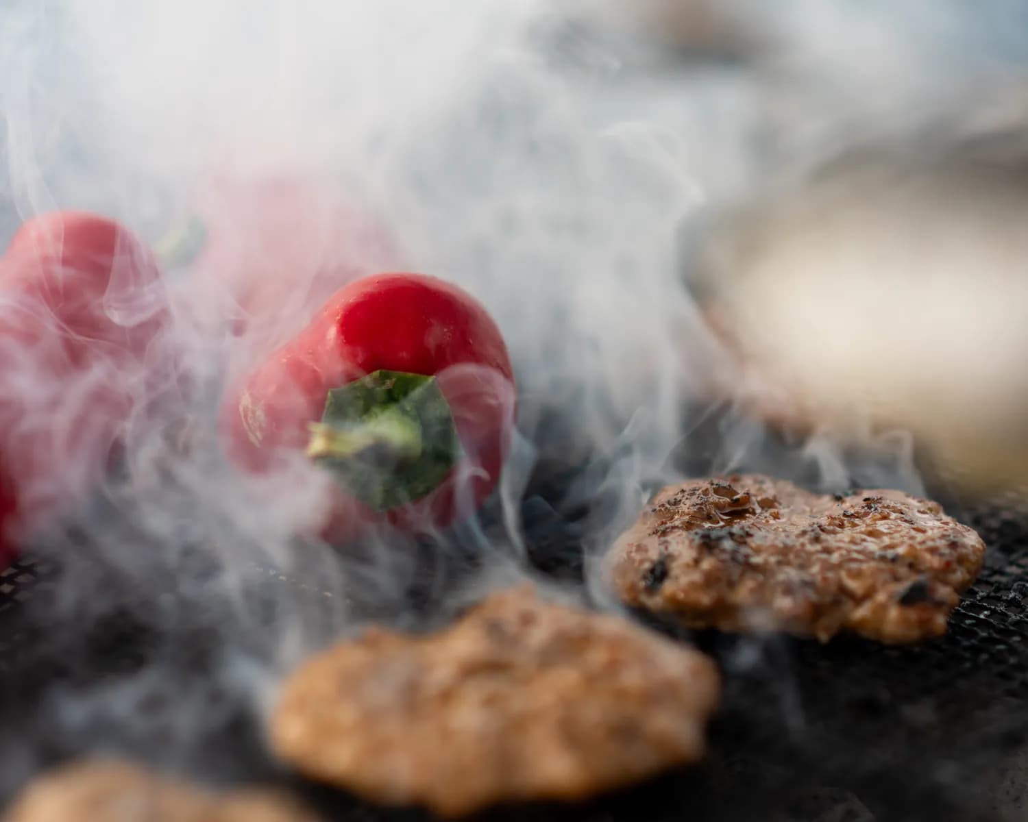Köfte und rote Peperoni im Rauch auf dem Kohlegrill